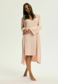 Jasnoróżowa sukienka z dekoltem w serek i krótkimi rękawami, zestawiona z dopasowanym długim kardiganem. Gładki materiał i swobodny krój, do kolan.