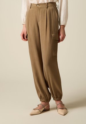 Brune cargobukser med høj talje, plisseringer og elastiske manchetter, båret med beige spidse flade sko med tynde stropper i slangeprint.