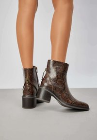 Bottes de cheville à motif serpent brun avec une surface texturée, fermetures éclair et un talon bloc. Met en valeur un design élégant et un matériau durable.