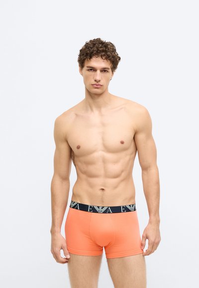 Boxers laranja com uma cintura azul marinho que apresenta um logótipo. O tecido parece macio, ajustado ao corpo e com textura suave.