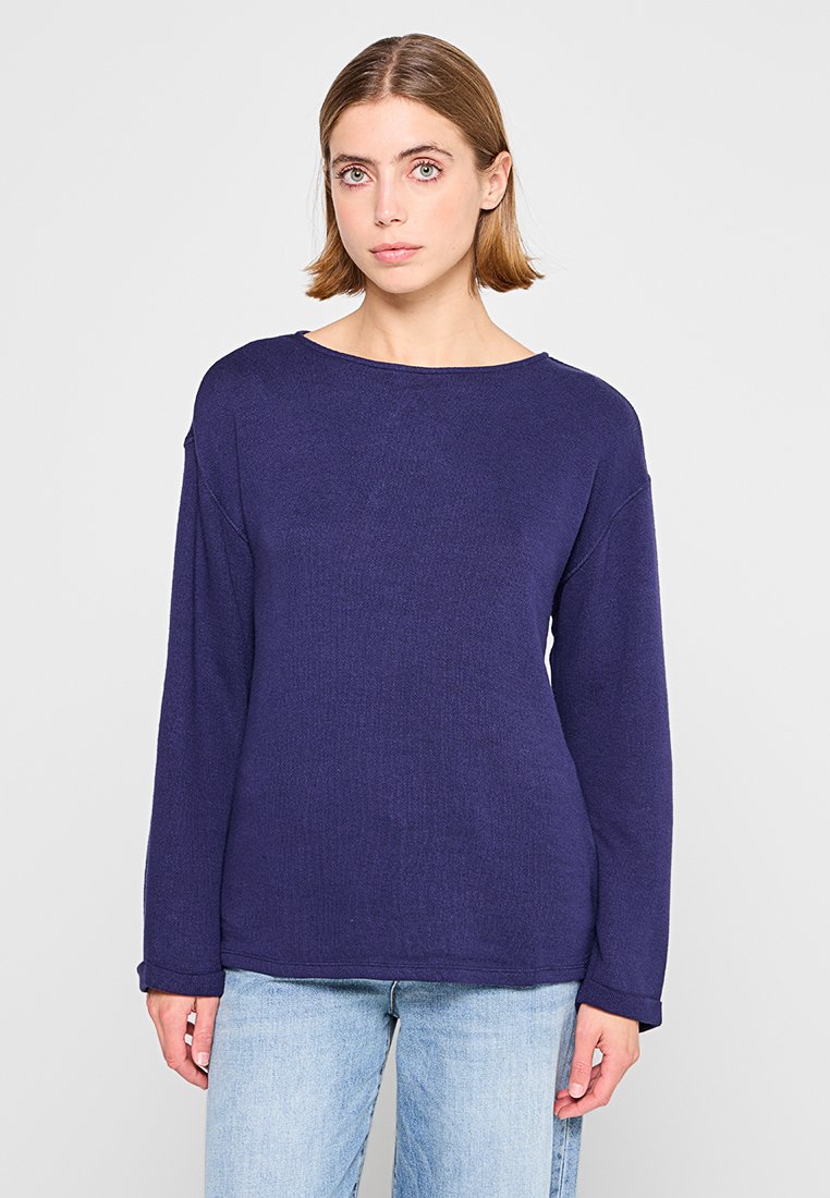 Haut à manches longues bleu marine avec un grand col, texture côtelée, coupe détendue et épaules tombantes, associé à un jean bleu clair.