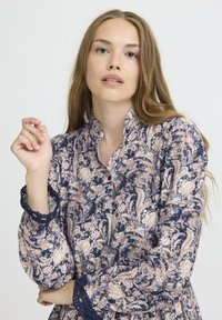 Garā piedurkņu ziedu kleita ar tumši zilas krāsas pamatu un rozā un krēmkrāsas rakstiem. Tekstūras mežģīņu apdare uz Piedurkņu galiem un mandarina apkakles.