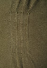 Gros plan sur un tissu vert olive avec quatre rangées verticales de coutures détaillées sur une surface texturée.