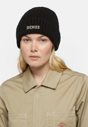 Musta ribattu pipo, jossa on neulepinta, ja jonka etuosassa on beige kirjailtu "DICKIES" -logo; käytetään beige kauluspaitaan yhdistettynä.