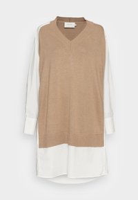 Pull en tricot beige avec un col en V, manches longues blanches contrastantes et un ourlet présentant une texture côtelée. Design superposé sophistiqué.