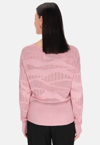 Pulover tricotat de culoare roz deschis cu un model în valuri. Are un tiv și mansete ribelate, mâneci lungi și un design cu spatele deschis.