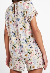 Blumiges Schlafanzug-Set mit einem cremfarbenen Hintergrund und bunten Blüten, kurzen Ärmeln und einem Schlüsselloch-Ausschnitt auf der Rückseite. Weicher, leichter Stoff.