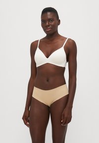 Reggiseno a coppa bianca modellata con spalline sottili regolabili abbinato a slip hipster beige senza cuciture. Tessuto liscio, design minimalista, senza hardware visibile.