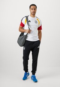 Herresportswear bestående af en hvid, rød og gul kortærmet skjorte med Tysklands logo, sorte bukser og blå træningssko.