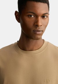 T-shirt beige a maniche corte realizzata in materiale morbido, con scollatura rotonda e un piccolo logo ricamato sul petto.