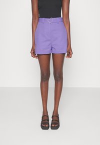 Purple high-waisted shorts with a triangle buckle belt, featuring a tailored design and smooth fabric. Paired with black strappy sandals.