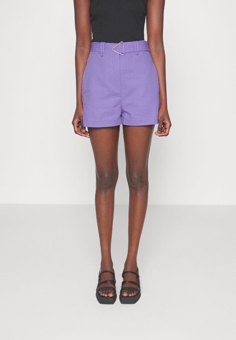 Purple high-waisted shorts with a triangle buckle belt, featuring a tailored design and smooth fabric. Paired with black strappy sandals.