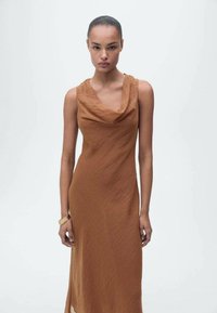 Cowl-neck, sleeveless dress in a warm, brown fabric with a subtle texture, featuring a flowing silhouette and a mid-calf length.