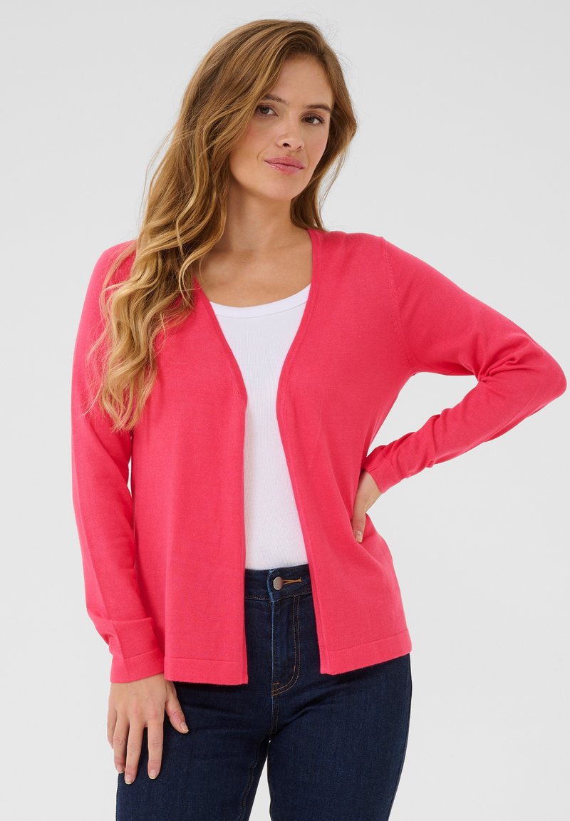 Roze cardigan met lange mouwen, een open voorkant en een zachte textuur, gedragen over een wit topje en gecombineerd met donkerblauwe jeans.