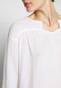 Tunique blanche légère au look décontracté, dotée d'un large col et d'une subtile texture verticale. Le tissu semble doux et respirant.