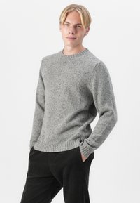 Gray knitted sweater with a crew neckline, textured surface, and ribbed cuffs and hem, paired with dark corduroy pants.