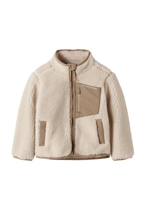 Veste polaire couleur crème avec fermeture éclair marron et détails sur les poches, col montant et texte « Studio Outdoors » sur la poche poitrine.