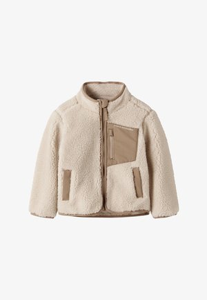 Veste polaire couleur crème avec fermeture éclair marron et détails sur les poches, col montant et texte « Studio Outdoors » sur la poche poitrine.