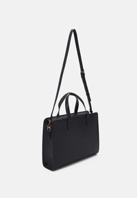 Černá obdélníková ramenní taška s dvěma držadly a nastavitelným dlouhým popruhem, vystavená na jednobarevném bílém pozadí.