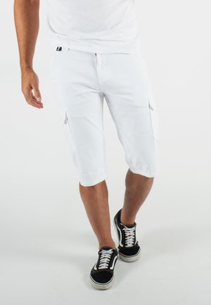 Shorts cargo blancs arrivant au genou avec des poches latérales, associés à des baskets noires avec des lacets blancs. Tissu en coton, design décontracté.