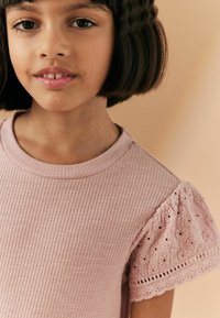 Ljusrosa ribbad t-shirt med korta puffärmar som har blommig hålmönstrad spets och rund halsringning.