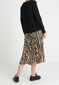 Haut à manches longues noir associé à une jupe plissée avec un motif rayé beige et noir. Des chaussures noires à lacets complètent la tenue.