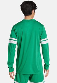 T-shirt de sport long vert à manches longues avec des rayures blanches sur les manches. Texture légère et lisse avec un col arrondi et une coupe décontractée.