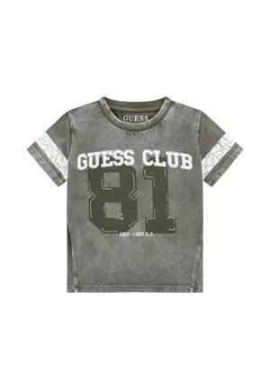 T-shirt vert olive en coton biologique, arborant un imprimé blanc craqué avec "GUESS CLUB" et "81" à l'avant, à manches courtes et col rond.