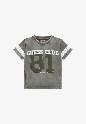 Olivově zelené tričko vyrobené z organické bavlny, s popraskaným bílým potiskem "GUESS CLUB" a "81" na přední straně, krátké rukávy a kulatý výstřih.