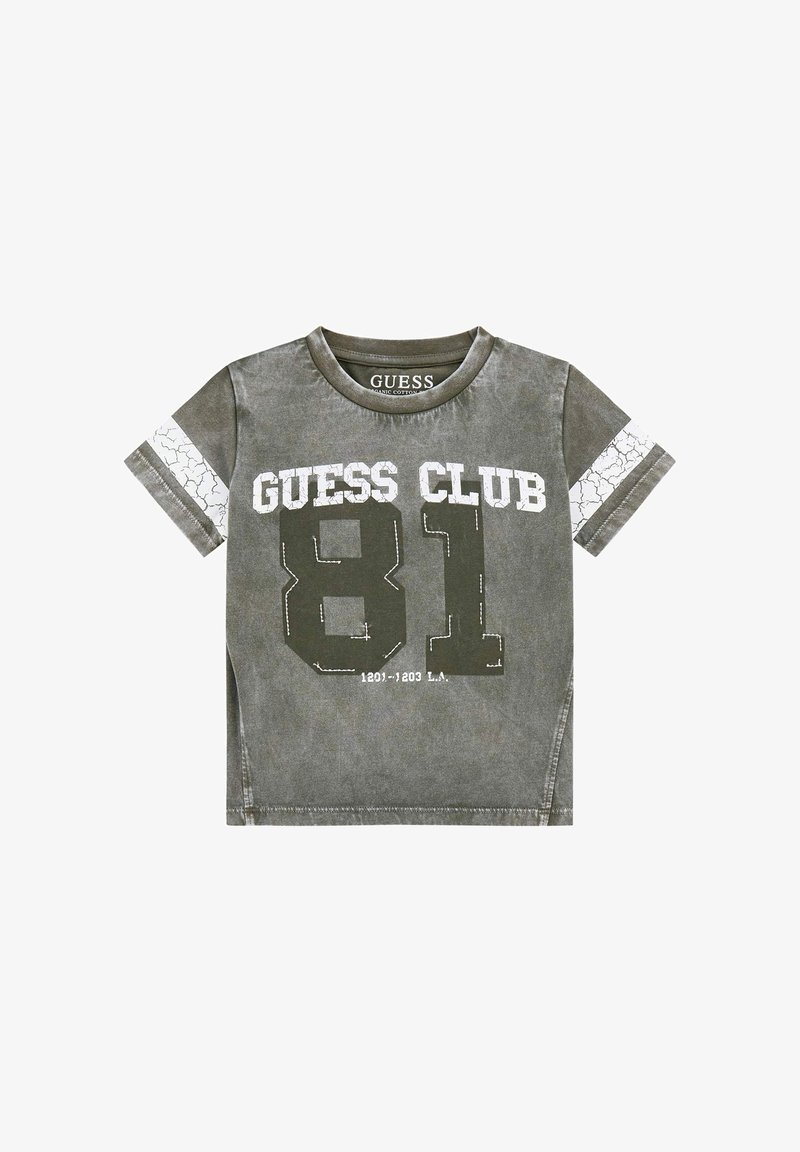 Olīvu zaļš T-krekls, kas izgatavots no organiskās kokvilnas, ar krekinga balto printu "GUESS CLUB" un "81" priekšpusē, īsām piedurknēm un apaļu kakla izgriezumu.