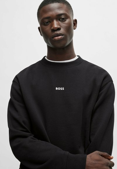 Sweatshirt noir en tissu texturé, avec un col rond et un logo "BOSS" blanc sur la poitrine. Manches ajustées et coupe décontractée.