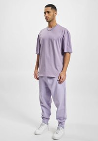 Fioletowa, bawełniana, oversizowa koszulka z krótkim rękawem w zestawie z dopasowanymi dresami. Białe sneakersy dopełniają całość. Prosty design i luźny krój.