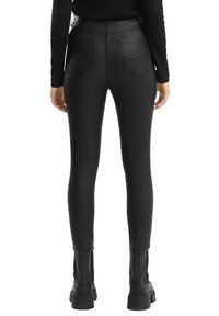 Leggings taille haute en simili cuir noir avec une texture lisse, une silhouette ajustée et deux poches arrière. Associés à des bottines noires.
