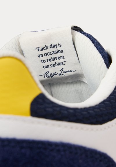 Ετικέτα με ρήση μέσα σε ένα ναυτικό, λευκό και κίτρινο αθλητικό παπούτσι που λέει, «Κάθε μέρα είναι μια ευκαιρία να ανανεώσουμε τον εαυτό μας.» - Ραλφ Λόρεν.