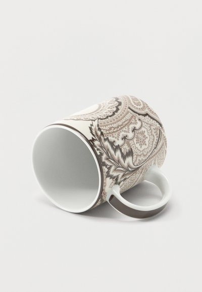 Tasse à café en porcelaine avec des motifs floraux et cachemire complexes en beige et marron, posée sur le côté sur une surface blanche.