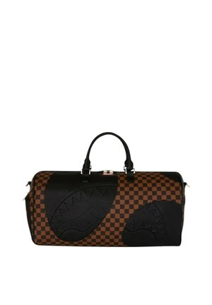 Grande borsa da viaggio marrone e nera a quadri con disegni di facce di squalo nere e manici neri su sfondo bianco.