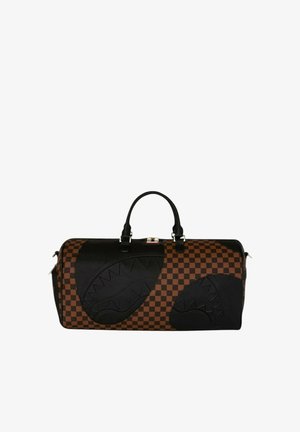 Grande borsa da viaggio marrone e nera a quadri con disegni di facce di squalo nere e manici neri su sfondo bianco.