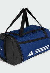 Marineblå duffelbag med sorte detaljer, lynlåslukning og topgreb. Har hvidt logo og striber på siden. Tekstureret stof.