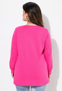 Camiseta de manga larga rosa en tejido suave, con cuello redondo y corte holgado, combinada con jeans de denim ligeramente desgastados.