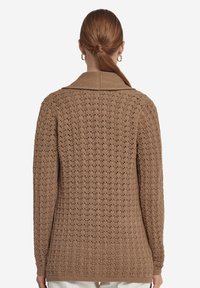 Brun stickad cardigan med ett strukturerat mönster, som har en krage och långa ärmar, som sträcker sig till höfterna.