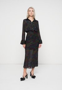 Μαύρο φόρεμα με γιακά, διακοσμημένο με πολύχρωμες βούλες, μακριά μανίκια και βολάν στις μανσέτες, σε συνδυασμό με μαύρες ψηλές γόβες.