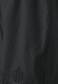 Černá látková sukně s květinovou výšivkou na spodním lemu, se složitými výřezy. Měkká textura a splývavý design.