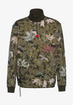 Tröja med hög krage i brunt, med ett blommönster i rosa, vitt och grönt på en olivgrön kamouflagebakgrund, med dragkedja framtill.