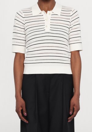 White knitted short-sleeve polo with horizontal black stripes and cut-out patterns. Three-button placket and ribbed hem. Worn with black pants.