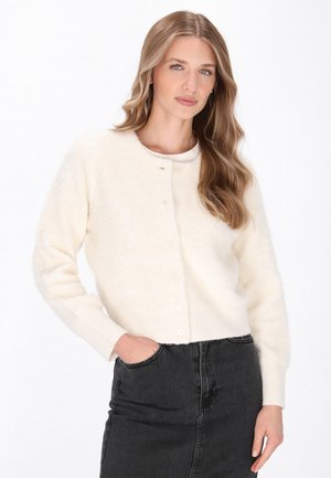 Cardigan bianco e soffice con scollo rotondo e chiusura con bottoni frontali. Presenta polsini e orlo a coste. Indossato con una gonna di jeans nera.