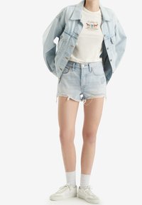 Chaqueta de mezclilla azul claro, camiseta crema con gráfico, pantalones cortos desgastados azul claro, calcetines blancos y zapatillas blancas. Conjunto de ropa casual.