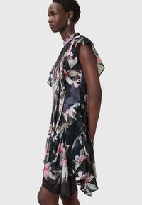 Schwarz-blumenkleid mit rüschenärmeln, tailliertem Oberteil und ausgestellt Rock mit rosa und grünen botanischen Mustern.