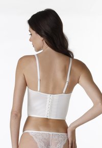 Camisola bianca in satin con sottili spalline regolabili, dotata di chiusura posteriore a gancetto e superficie liscia.