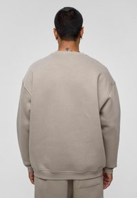 Beige oversized sweatshirt met een gestructureerde afwerking. Heeft verlaagde schouders, een ronde hals en geribde manchetten. Geen zichtbare merknaam of patronen.