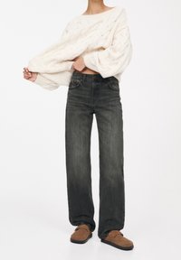 Maglione bianco a trecce, jeans scuri a vita alta e scarpe slip-on marroni. La vestibilità è rilassata con una silhouette ampia e texture morbida.